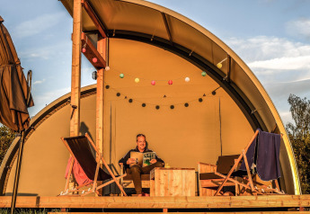 Person entspannt und liest in einem Luxus-Glampingzelt im Holiday Park Mölke in den Niederlanden bei Sonnenuntergang.