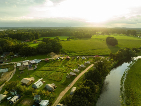 Vue aérienne de tentes glamping de luxe au Holiday Park Mölke, Pays-Bas, entourées de champs et d’une rivière.
