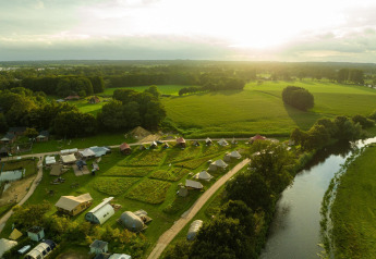 Vista aerea delle tende di glamping di lusso al Holiday Park Mölke, Paesi Bassi, accanto ai campi e al fiume.