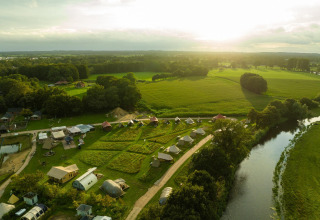 Vue aérienne de tentes glamping de luxe au Holiday Park Mölke, Pays-Bas, entourées de champs et d’une rivière.