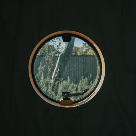 Rond raam in Wikkel tiny house bij De Klepperstee, Nederland, met uitzicht op tuin en schutting.
