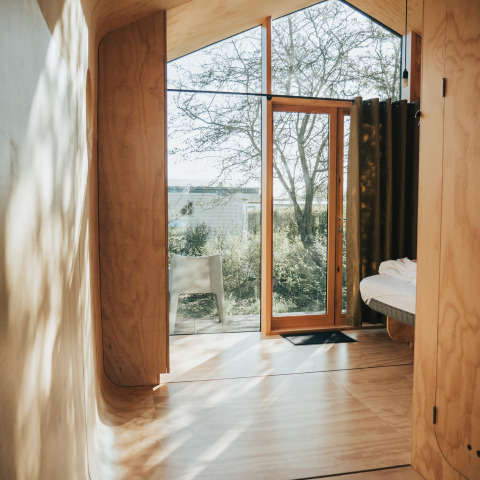 Interior de la casa diminuta Wikkel en Holiday park De Klepperstee con madera y grandes ventanales.