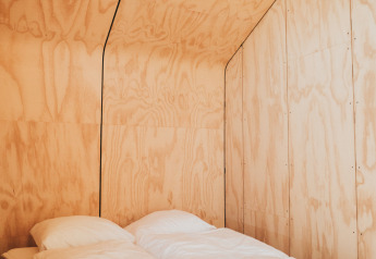 Interno minimalista in legno con letto doppio nella tiny house Wikkel, Holiday park De Klepperstee, Paesi Bassi.