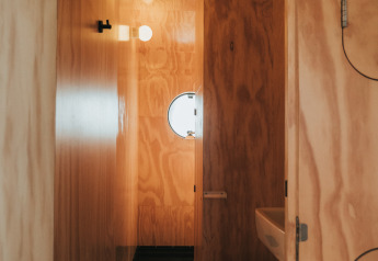 Houten badkamer in Wikkel tiny house op Holiday park De Klepperstee, Nederland, met een rond raampje.