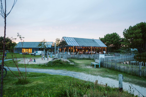 Glampingverblijf met houten lodges, zandbak, tuinbanken en een groene omgeving bij het vallen van de avond.