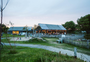 Glamping-accommodatie met moderne houten lodges, een zandbak, tuinbanken en een groene omgeving bij schemer.