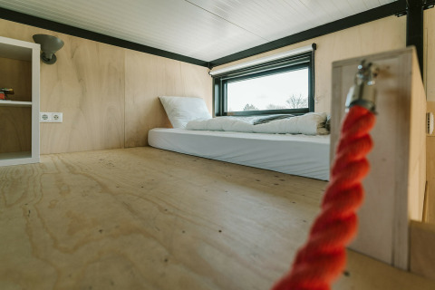 Interieur van tiny house-slaapruimte met matras, houten wanden en raam in De Klepperstee, Nederland.