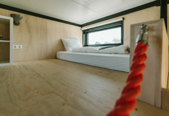Interieur van tiny house-slaapruimte met matras, houten wanden en raam in De Klepperstee, Nederland.