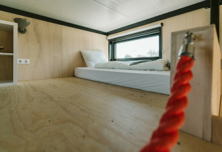 Interior de una casa pequeña con colchón en el piso, paredes de madera y ventana en De Klepperstee, Países Bajos.