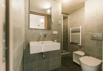Salle de bain moderne avec carrelage gris, WC suspendu, lavabo, douche et miroir dans une tiny house.
