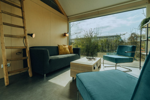 Sala moderna en una cabaña del Holiday Park De Klepperstee, Países Bajos, con amplios ventanales y muebles elegantes.
