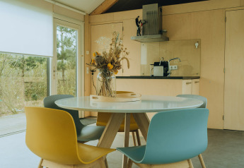 Eethoek met gekleurde stoelen en een ronde tafel in een moderne lodge op vakantiepark De Klepperstee, Nederland.