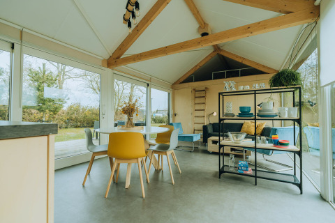 Modern lodge-interieur met eettafel, gele stoelen en grote ramen bij t Kroaje, De Klepperstee, Nederland.