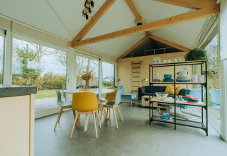 Modern lodge-interieur met eettafel, gele stoelen en grote ramen bij t Kroaje, De Klepperstee, Nederland.