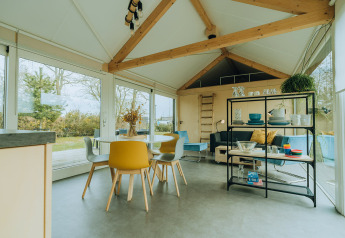 Modern lodge-interieur met eettafel, gele stoelen en grote ramen bij t Kroaje, De Klepperstee, Nederland.