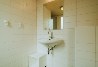 Baño moderno con azulejos blancos, lavabo de pared y espejo en De Klepperstee, Países Bajos.