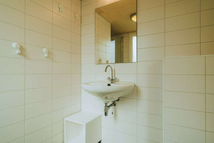 Modernes, weiß gefliestes Bad mit Wandwaschbecken und Spiegel in der Lodge ’t Kroaje, Niederlande.