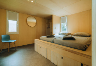Modernes Zimmer in der Lodge 't Kroaje im Ferienpark De Klepperstee, mit Holzwänden, Doppelbett und schlichter Einrichtung.
