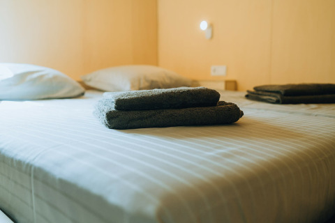 Two sets of dark towels folded neatly on a striped bed in t Kroaje lodge at De Klepperstee, Netherlands.