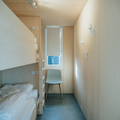 Minimalistische kamer met stapelbed, stoel en raam bij 't Kroaje, Holiday park De Klepperstee, Nederland.