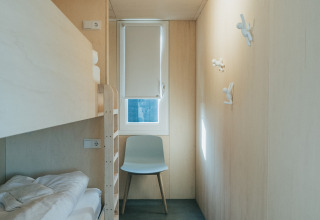 Habitación minimalista con litera, silla y ventana en 't Kroaje, Holiday park De Klepperstee, Países Bajos.