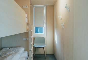 Minimalistische kamer met stapelbed, stoel en raam bij 't Kroaje, Holiday park De Klepperstee, Nederland.