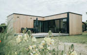 Moderne naturhytte i træ ved Holiday park De Klepperstee i Holland, omgivet af blomster og grønne planter.