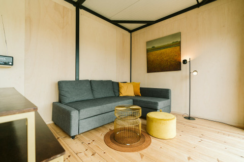 Moderne stue med grå hjørnesofa, gule puder og unikt sofabord i Huus van Hanse på De Klepperstee, Holland.