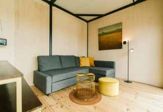 Moderne woonkamer met grijze hoekbank, gele kussens en uniek tafeltje in Huus van Hanse, De Klepperstee.