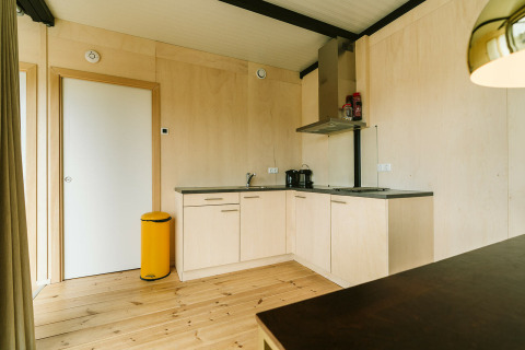 Coin cuisine moderne en bois clair avec poubelle jaune, Huus van Hanse, Holiday park De Klepperstee, Pays-Bas.