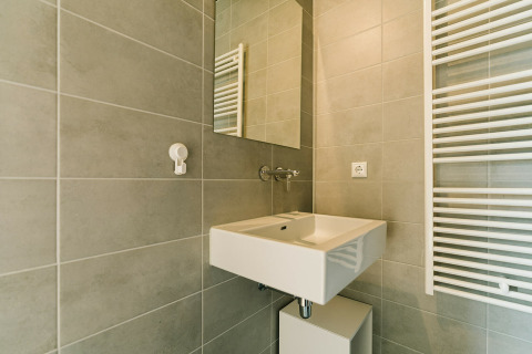 Baño moderno con azulejos grises, lavabo blanco, espejo y radiador toallero en una casa natural.