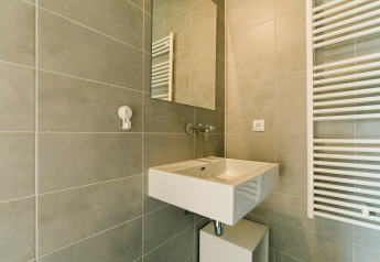 Moderne badkamer met grijze tegels, witte wastafel, spiegel en handdoekradiator in een natuurhuis.