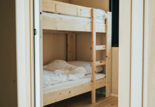 Lit superposé en bois clair dans une chambre chaleureuse à Huus van Hanse, maison nature au parc De Klepperstee.