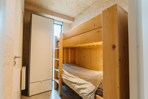 Dormitorio con litera de madera y armario blanco en Duunroos, parque vacacional De Klepperstee, Países Bajos.