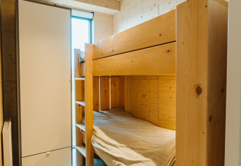 Lyst værelse med køjeseng af træ, skab og vindue i Duunroos-lodgen på Holiday park De Klepperstee.