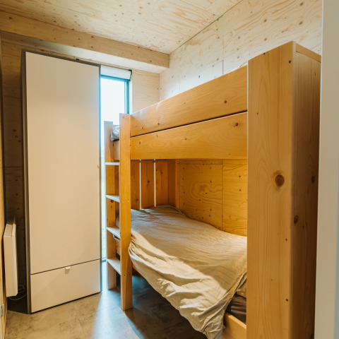 Lichte kamer met houten stapelbed, kast en raam in Duunroos lodge op vakantiepark De Klepperstee.