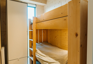 Lichte kamer met houten stapelbed, kast en raam in Duunroos lodge op vakantiepark De Klepperstee.