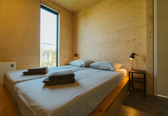 Moderne slaapkamer met houten wanden, twee bedden, lampjes en venster in Kleproos lodge op De Klepperstee, Nederland.