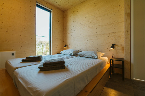 Moderne slaapkamer met houten wanden, twee bedden, lampjes en venster in Kleproos lodge op De Klepperstee, Nederland.
