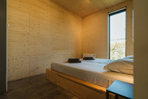 Dormitorio moderno en una cabaña de De Klepperstee, Países Bajos, con paredes de madera y cama iluminada.
