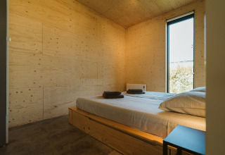 Dormitorio moderno en una cabaña de De Klepperstee, Países Bajos, con paredes de madera y cama iluminada.