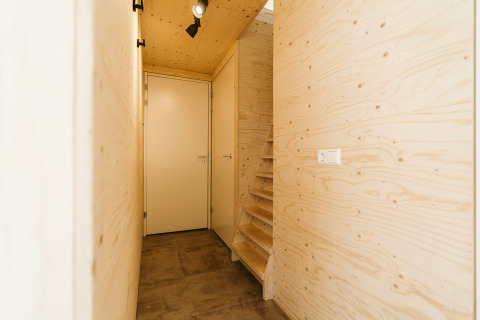 Pasillo de entrada en el lodge Kleproos en De Klepperstee con paredes de madera clara y una escalera estrecha.