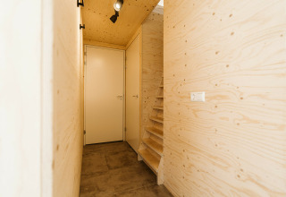 Pasillo de entrada en el lodge Kleproos en De Klepperstee con paredes de madera clara y una escalera estrecha.