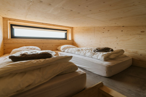 Deux lits simples avec linge blanc dans une chambre en bois du Lodge Kleproos, De Klepperstee, Pays-Bas.