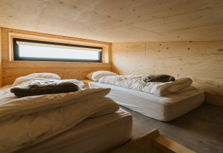Twee eenvoudige bedden met wit beddengoed in een houten kamer in Lodge Kleproos, De Klepperstee, Nederland.