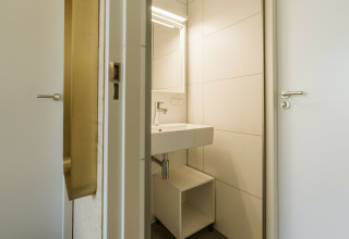 Baño moderno con lavabo blanco, espejo y estante en Kleproos, Holiday park De Klepperstee, Países Bajos.