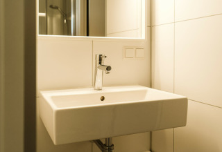 Moderne wastafel met spiegel en witte tegelwand in Kleproos, een lodge op vakantiepark De Klepperstee, Nederland.