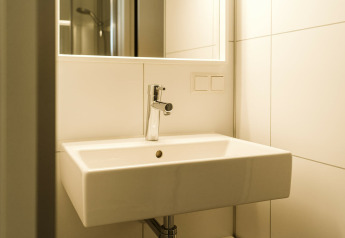 Moderne wastafel met spiegel en witte tegelwand in Kleproos, een lodge op vakantiepark De Klepperstee, Nederland.