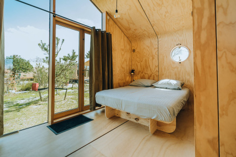 Modern wooden bedroom with large glass doors, double bed and view of nature at Oep, De Klepperstee, Netherlands.