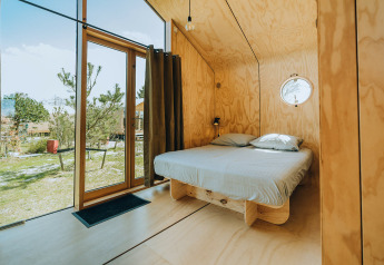 Moderne houten slaapkamer met tweepersoonsbed en grote ramen in natuurhuisje Oep, De Klepperstee, Nederland.